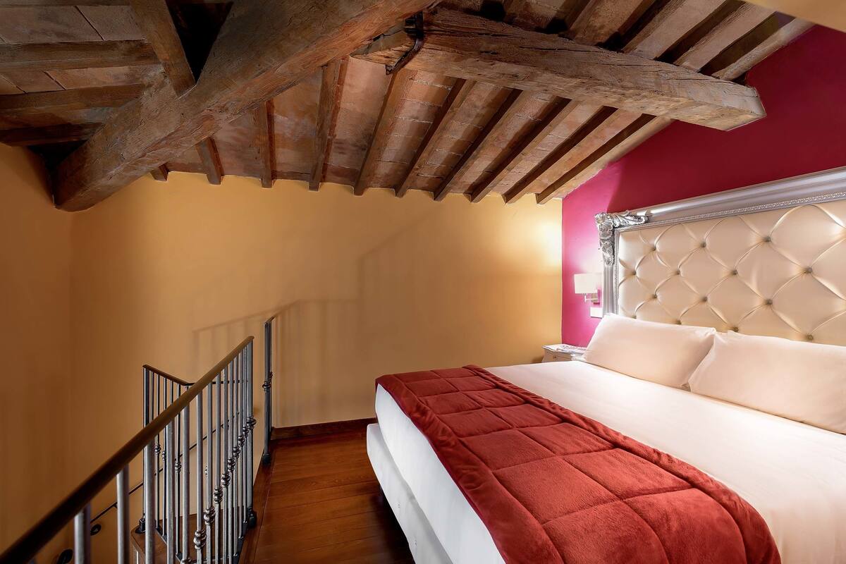 A bedroom with a wooden ceiling, a bed with a red blanket, and a white headboard.