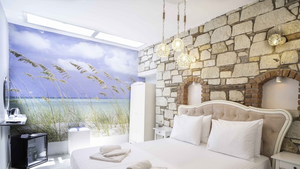 Un dormitorio con pared de piedra, una cama con ropa de cama blanca y vista al mar por una ventana.