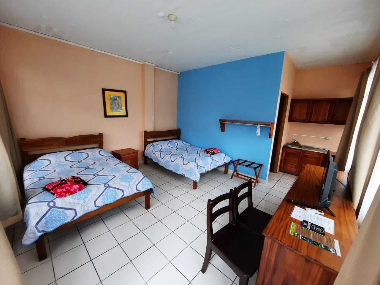 A hotel room with two beds, a desk, a chair, and a television.
