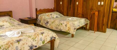 Habitación de hotel con dos camas, cabeceros de madera, cubrecamas estampados con motivos florales, un cuadro en la pared y un armario de madera.