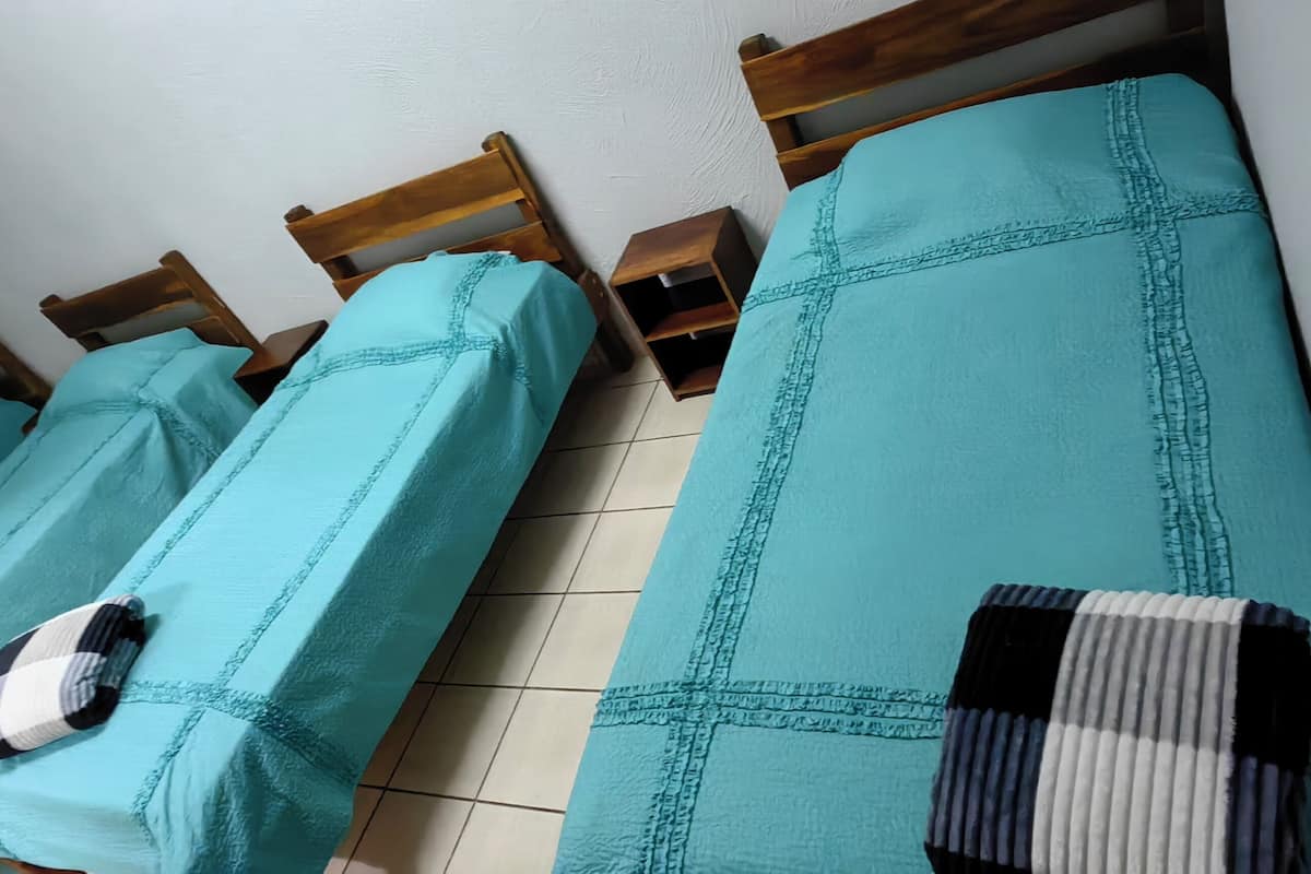 Une chambre avec quatre lits simples, chacun recouvert d’une courtepointe et doté d’oreillers de couleur turquoise.