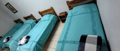 Ein Zimmer mit vier Einzelbetten, jedes mit einer türkisblauen Bettdecke und Kissen.