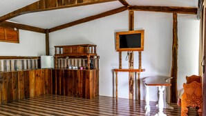 A rustic kitchen with wooden cabinets, a built-in refrigerator, a wooden bar counter, and a television mounted on a wooden stand.