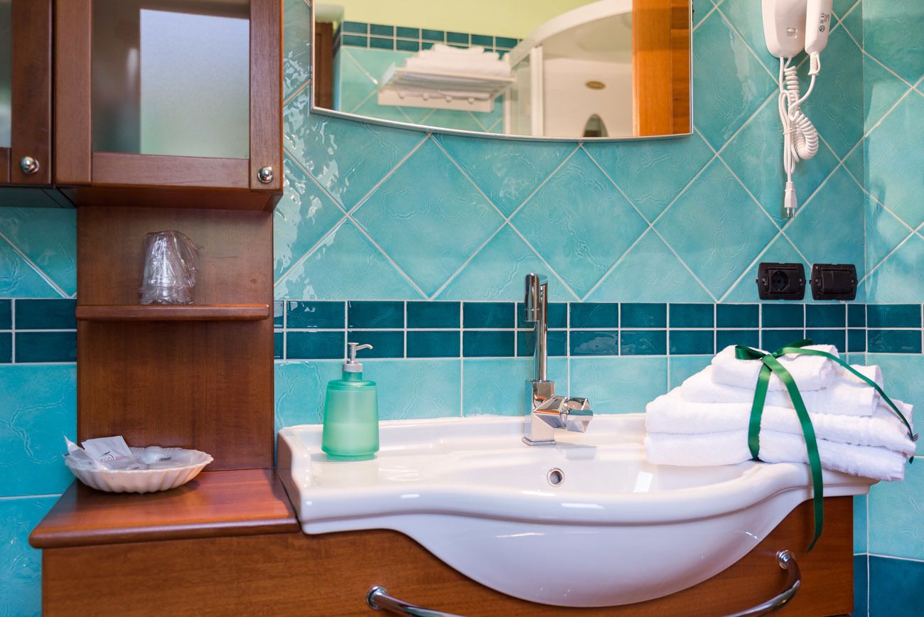 A bathroom with a white sink, a mirror, a towel rack, and a soap dispenser.