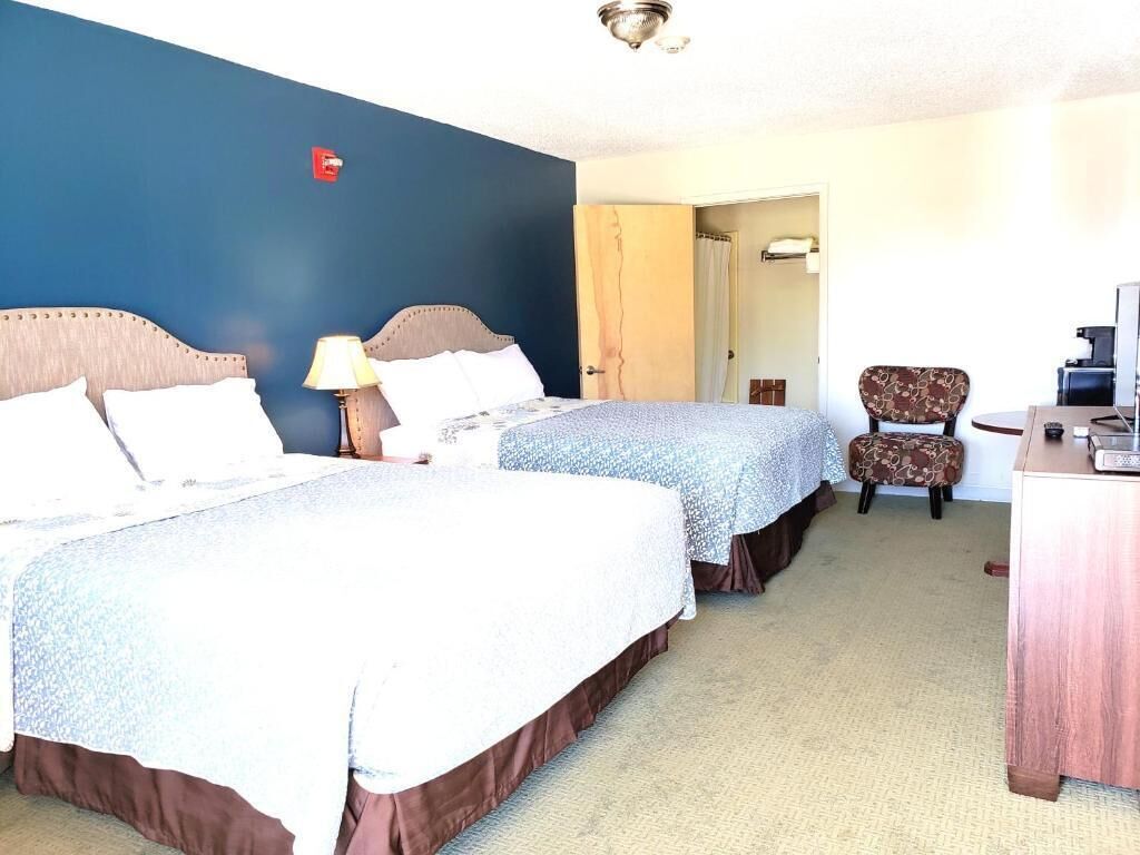 A hotel room with two beds, a desk, a chair, and a bathroom visible through an open door.