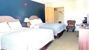 A hotel room with two beds, a desk, a chair, and a bathroom visible through an open door.