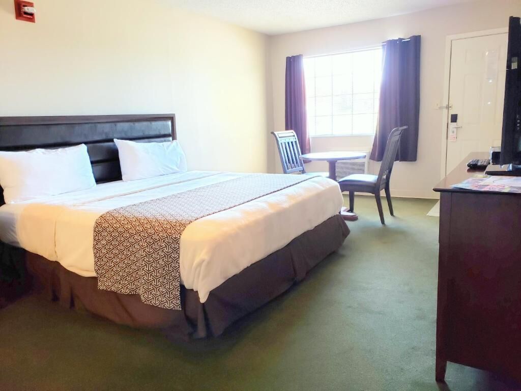 Habitación de hotel con cama, escritorio, silla y ventana con cortinas.