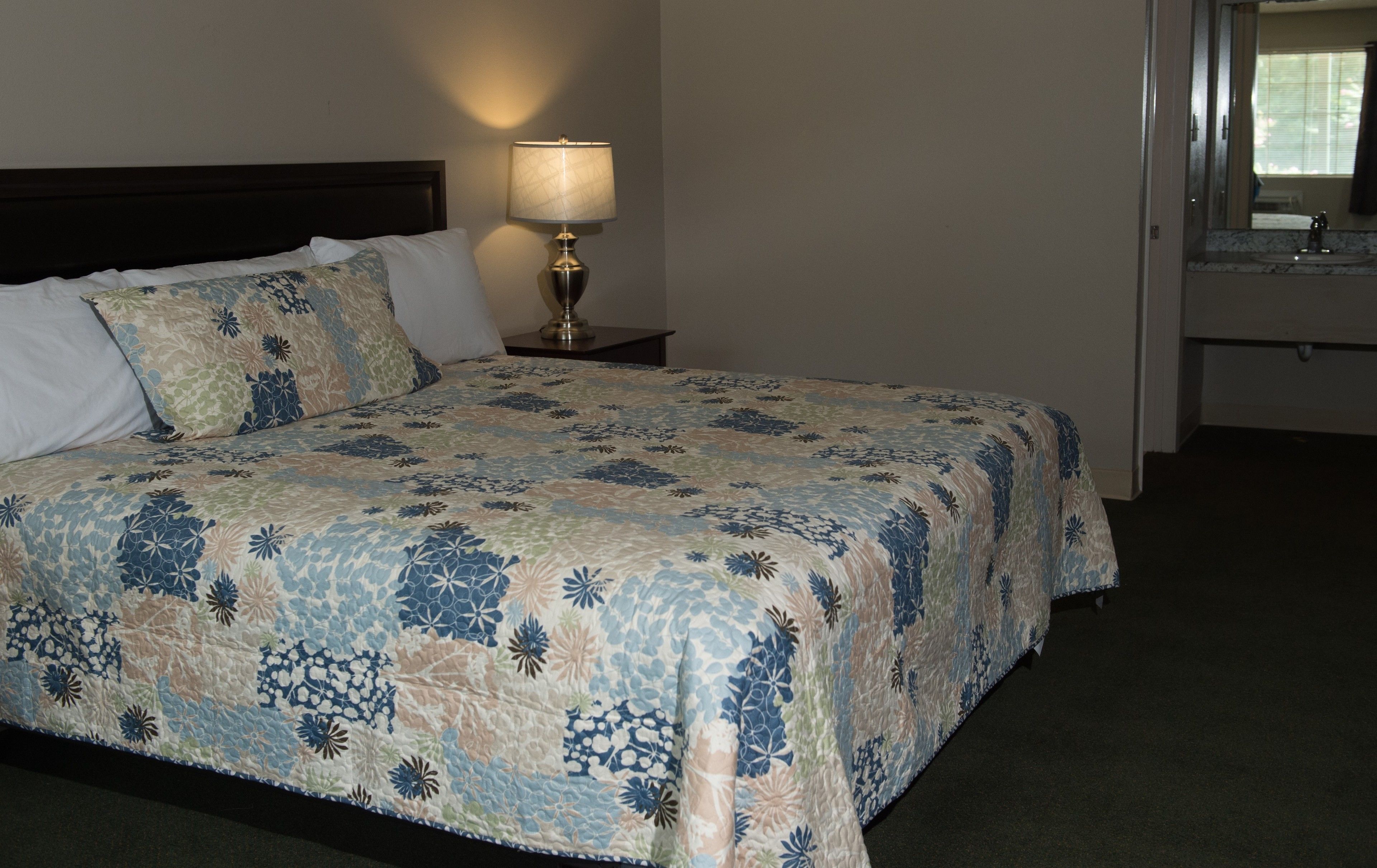 A neatly made bed with a floral-patterned bedspread, a bedside lamp, and a nightstand.