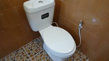 Toilet met een witte zitting en tank, voorzien van de tekst 'MOGEN', in een badkamer met bruine betegelde wanden en een mozaïek vloer.