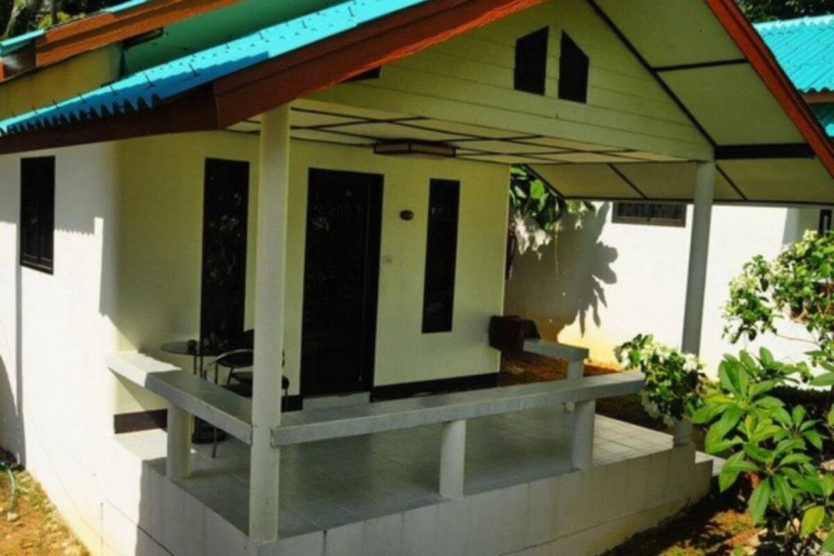 Um edifício térreo com varanda coberta, uma pequena área de estar ao ar livre e uma porta que dá para o interior.