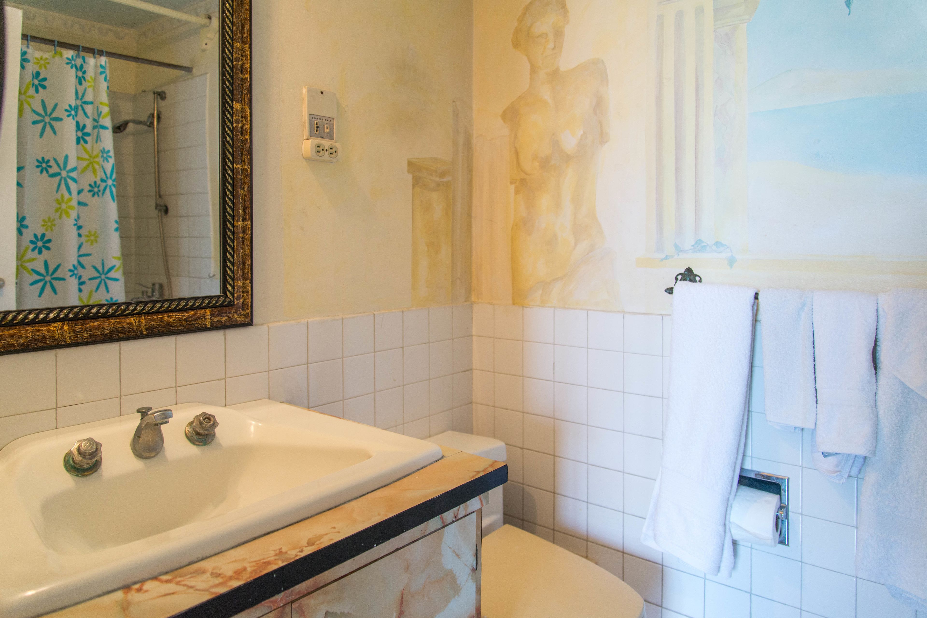 Een badkamer met een wit wastafelmeubel, een spiegel, een douche en een beeld aan de muur.