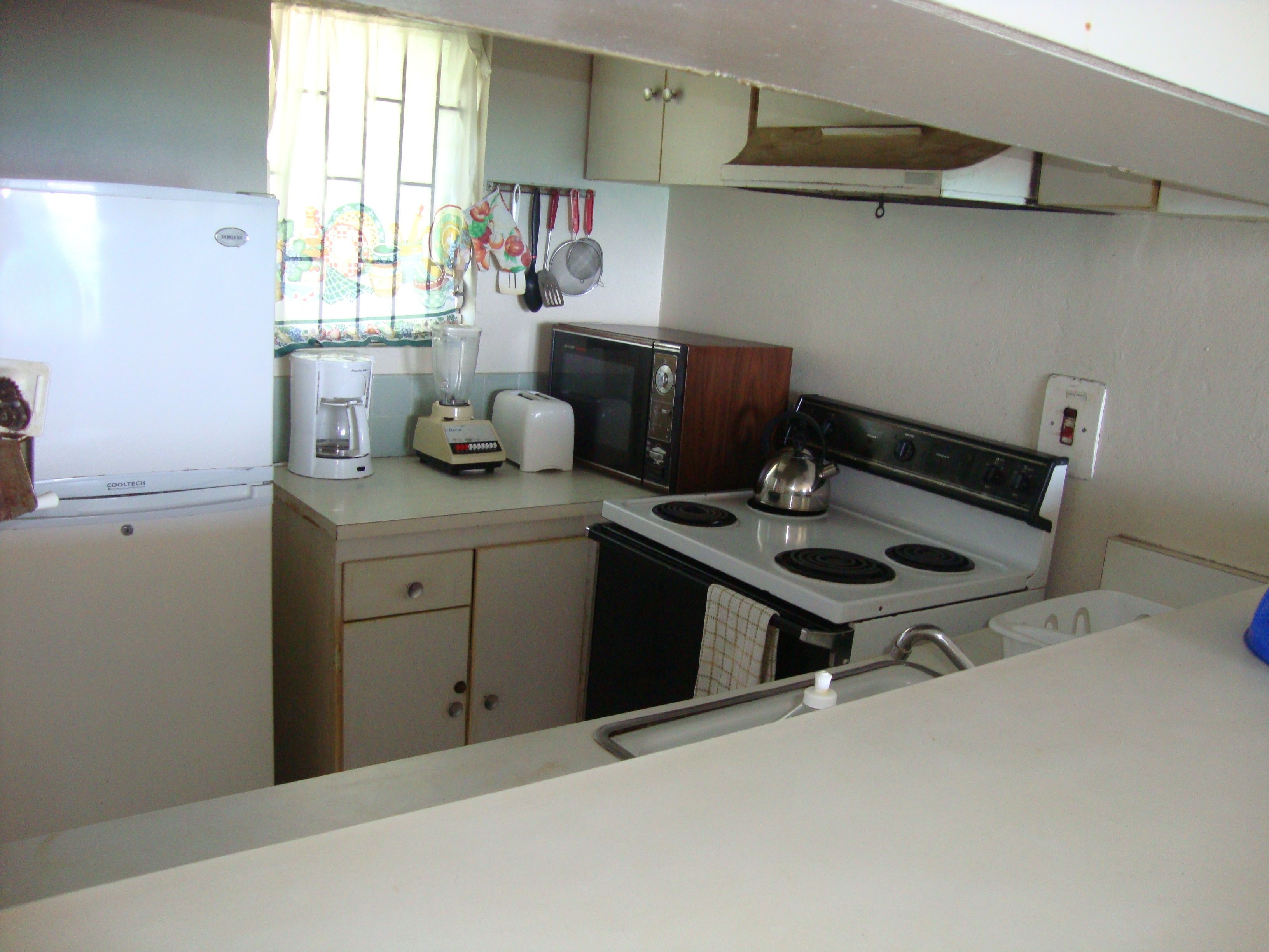 Una cocina compacta con refrigerador, estufa, microondas y varios electrodomésticos.