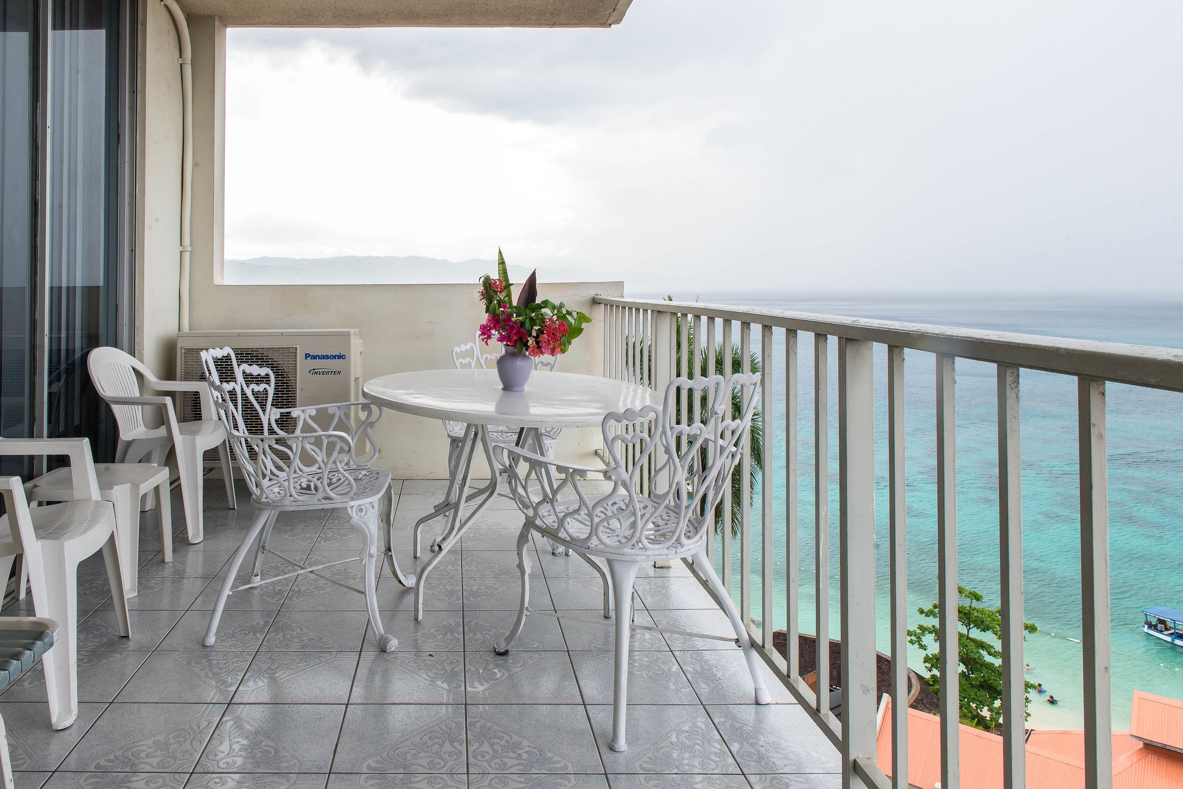 A balcony with a white table and chairs, a vase with flowers, and a view of the ocean.