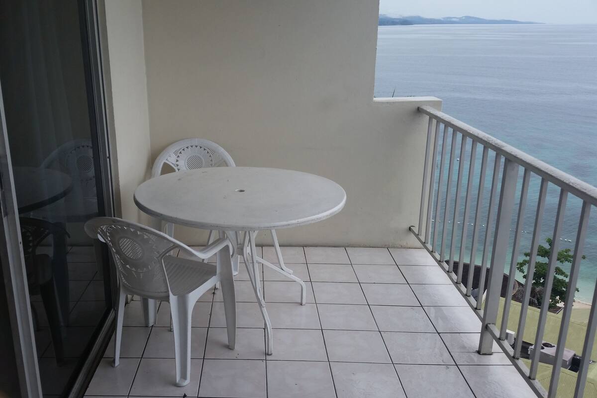 A balcony with a white table and chairs, a glass door, and a view of the sea.