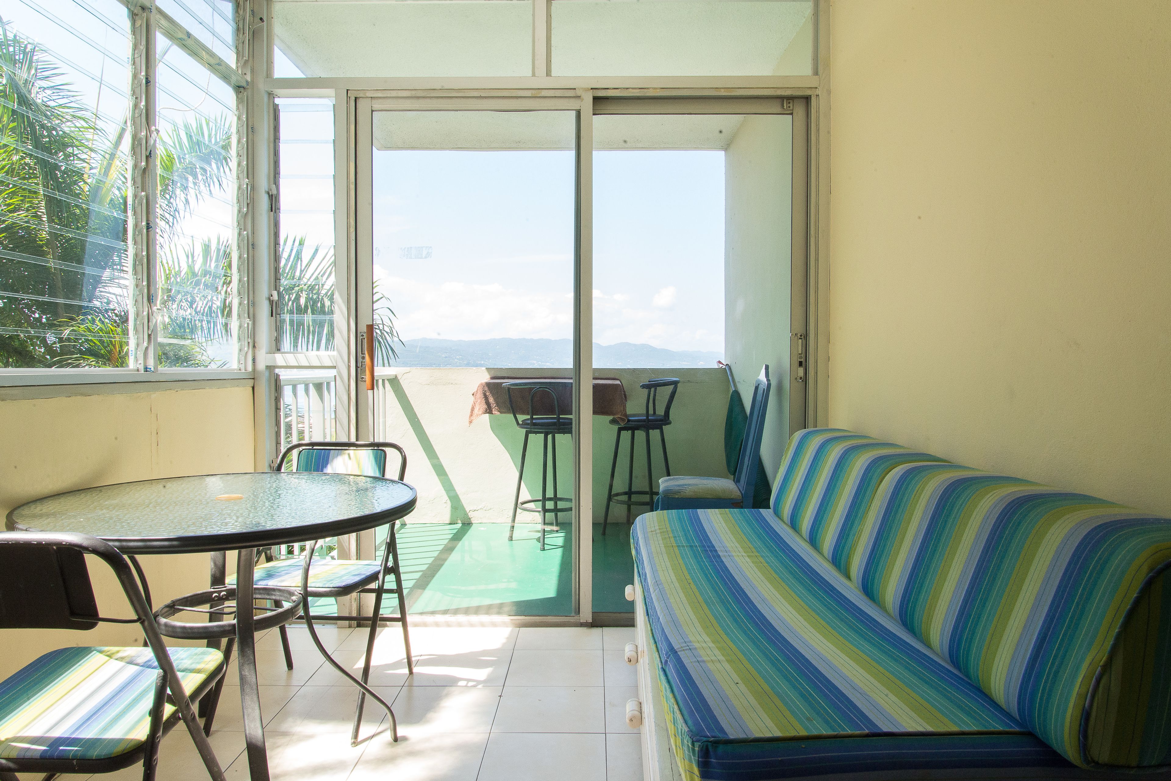 Een balkon met een glazen deur, een ronde tafel met stoelen en een gestreept bankje.