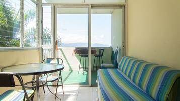 Een balkon met een glazen deur, een ronde tafel met stoelen en een gestreept bankje.