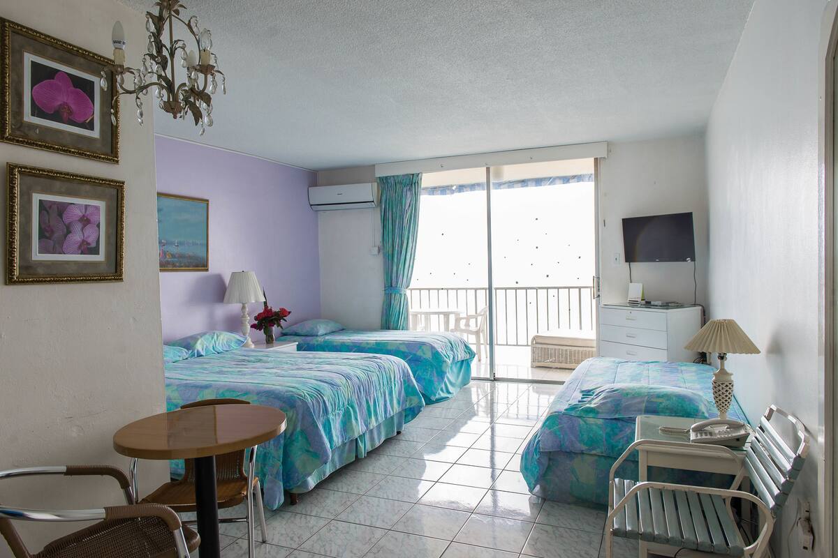 A hotel room with two beds, a table, chairs, a TV, and a balcony with a view.