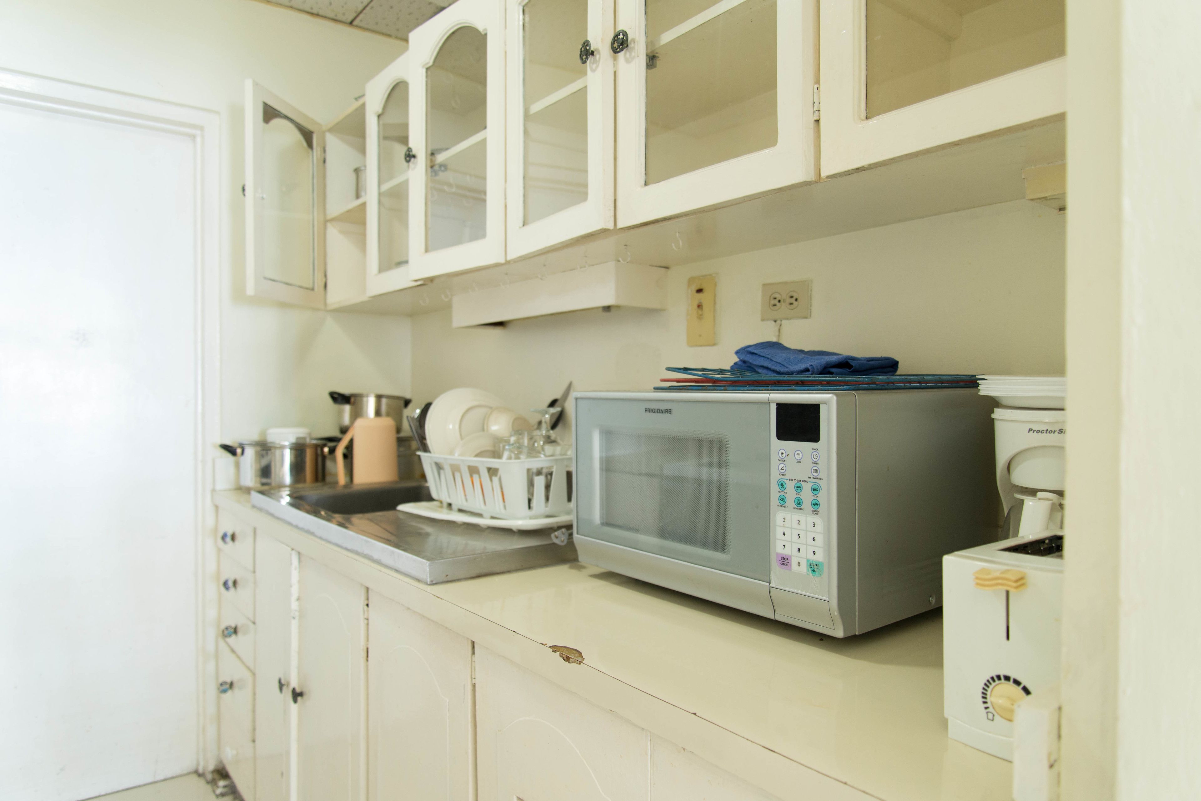 A kitchen with white cabinets, a microwave, a coffee maker, and a dish rack.