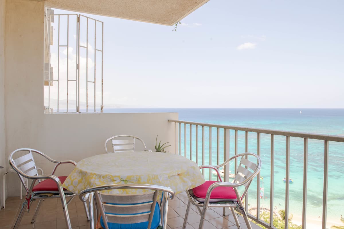 A balcony with a table and chairs, overlooking a clear blue sea.