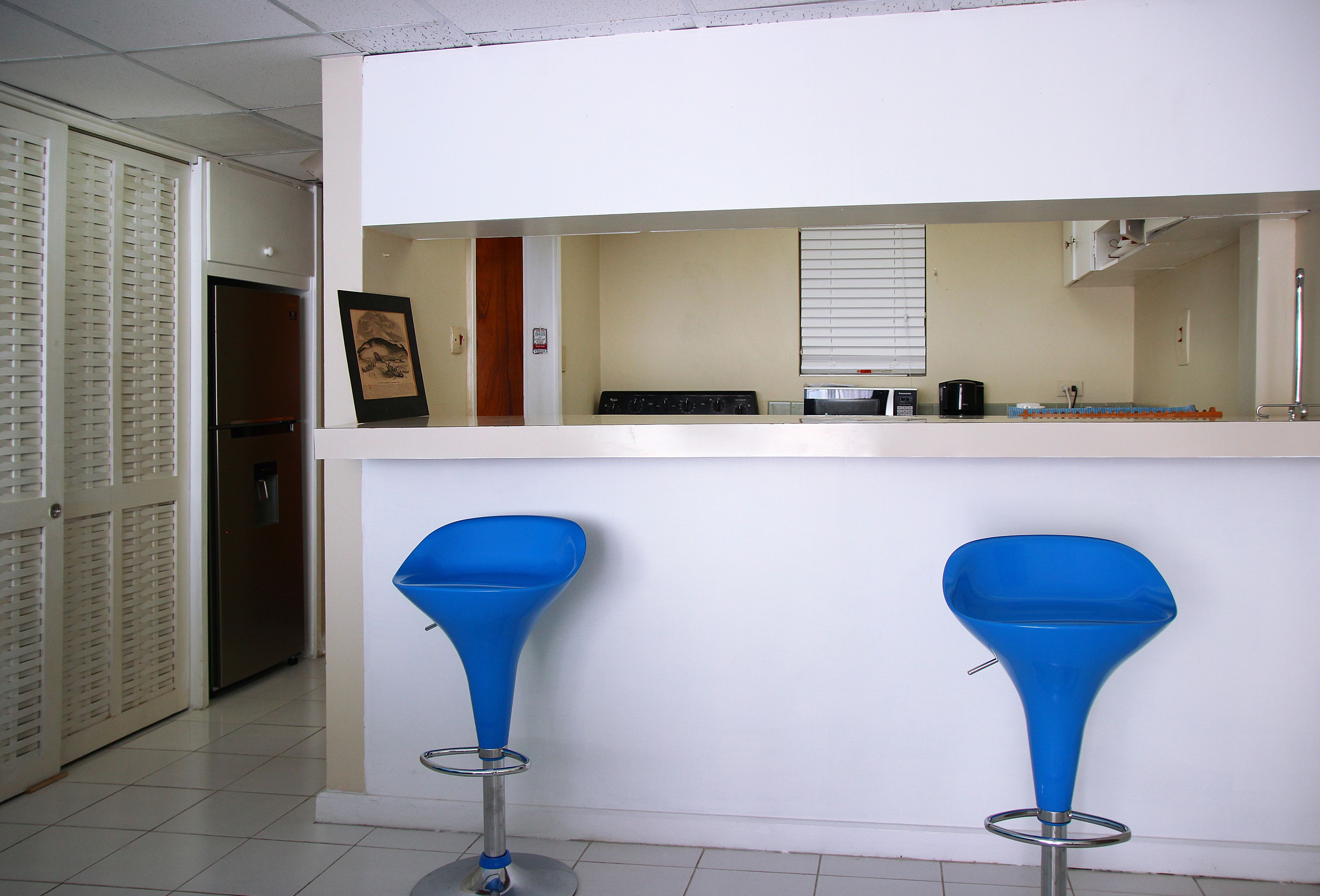 A kitchen with a refrigerator, stove, and microwave. There are two blue bar stools.