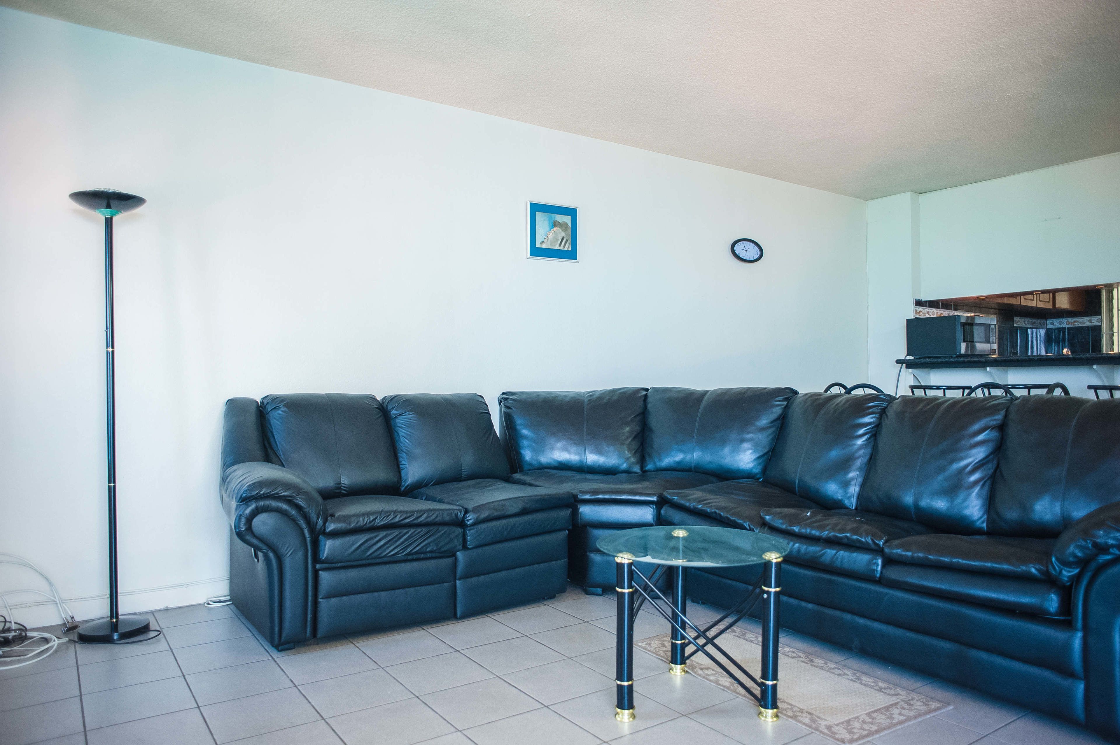 Un salon moderne avec un canapé d’angle, une lampe sur pied, une petite table et une horloge au mur.