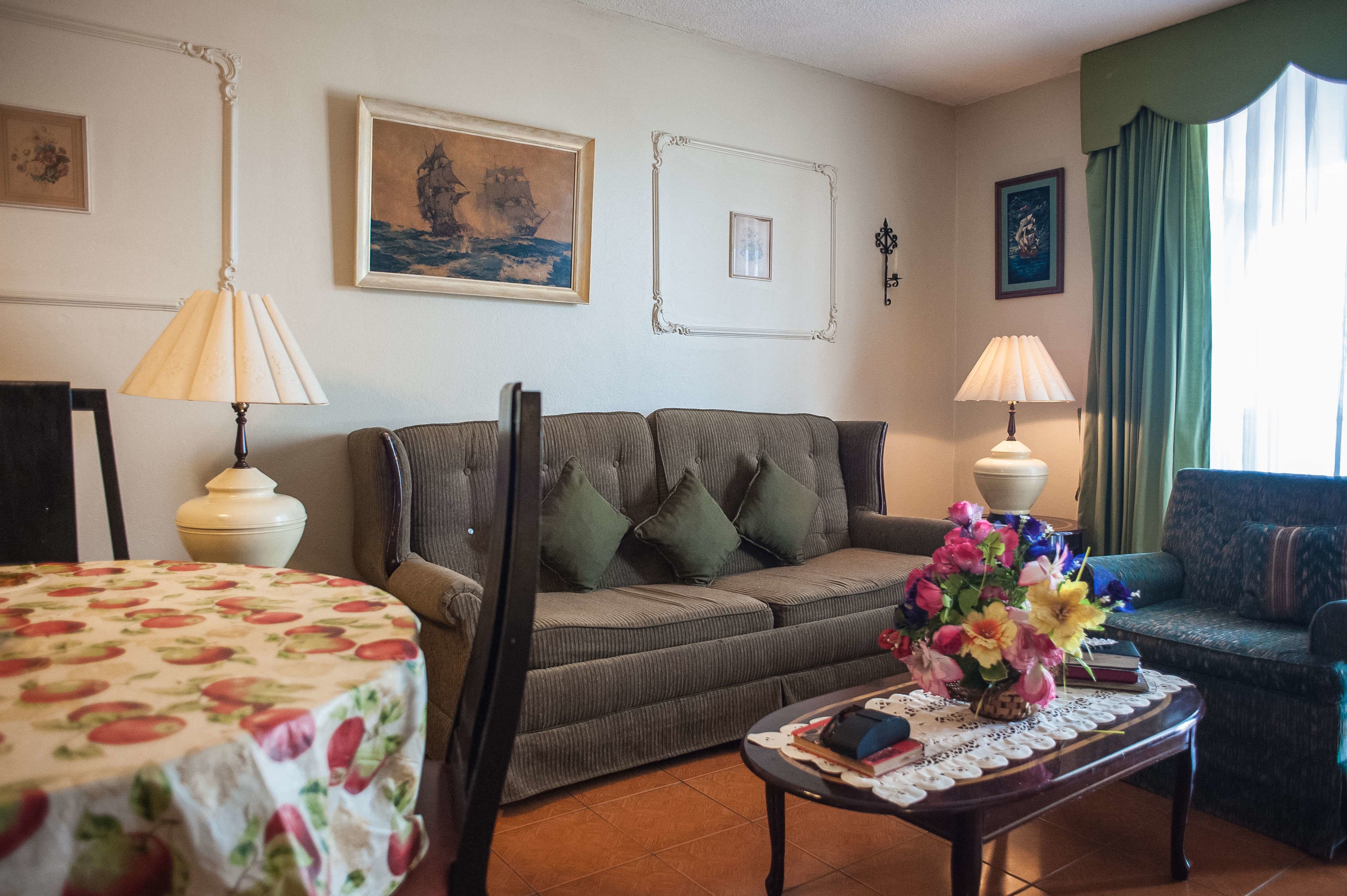 Ein Wohnzimmer mit einer Couch, zwei Lampen, einem Tisch mit Blumen in einer Vase und gerahmten Bildern an der Wand.