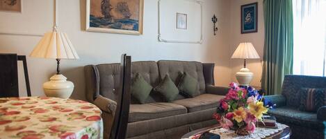 A living room with a sofa, two lamps, a table with a vase of flowers, and framed pictures on the wall.