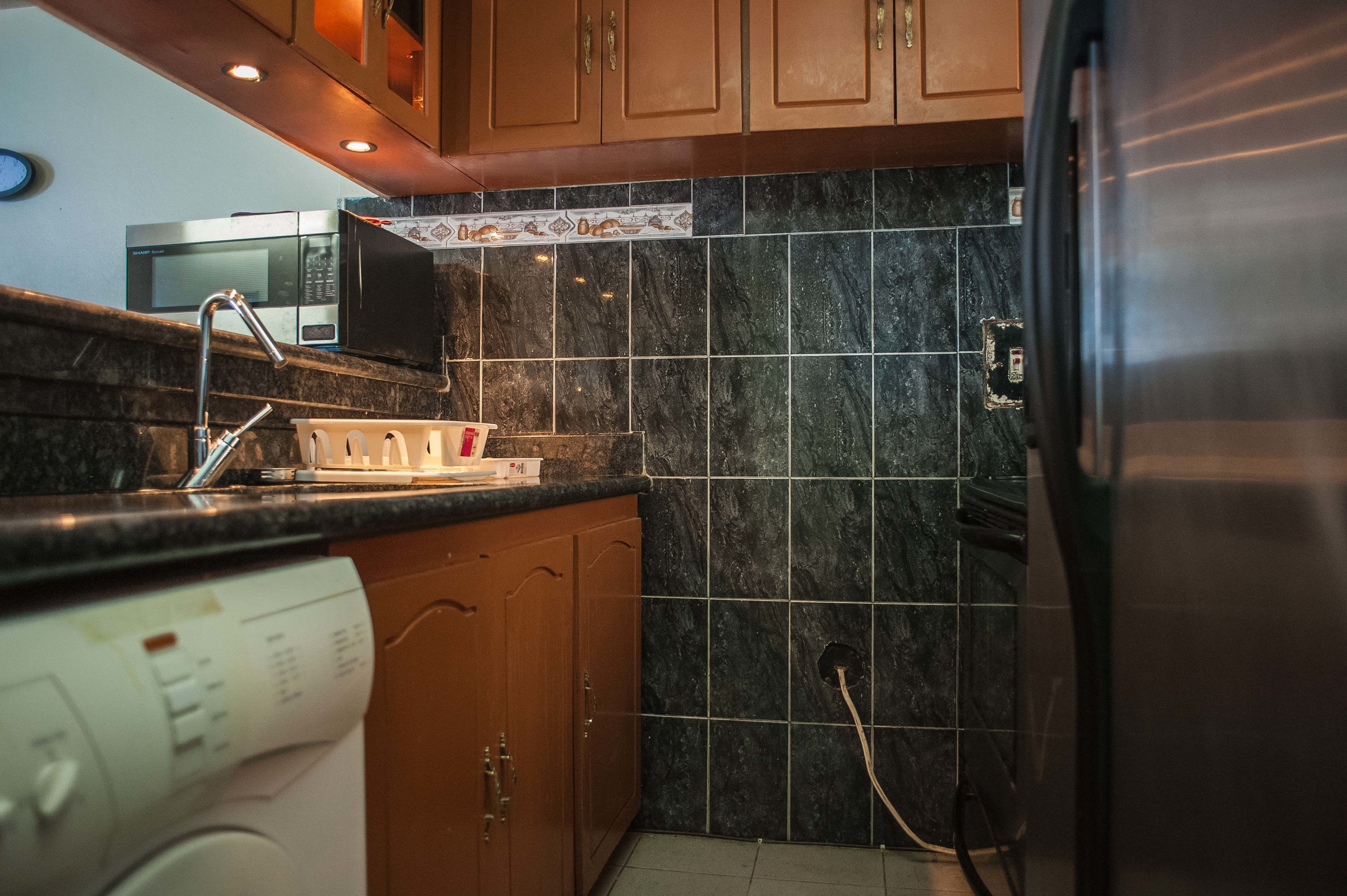 A kitchen with dark marble tiles, wooden cabinets, a stainless steel refrigerator, a microwave, and a dishwasher.