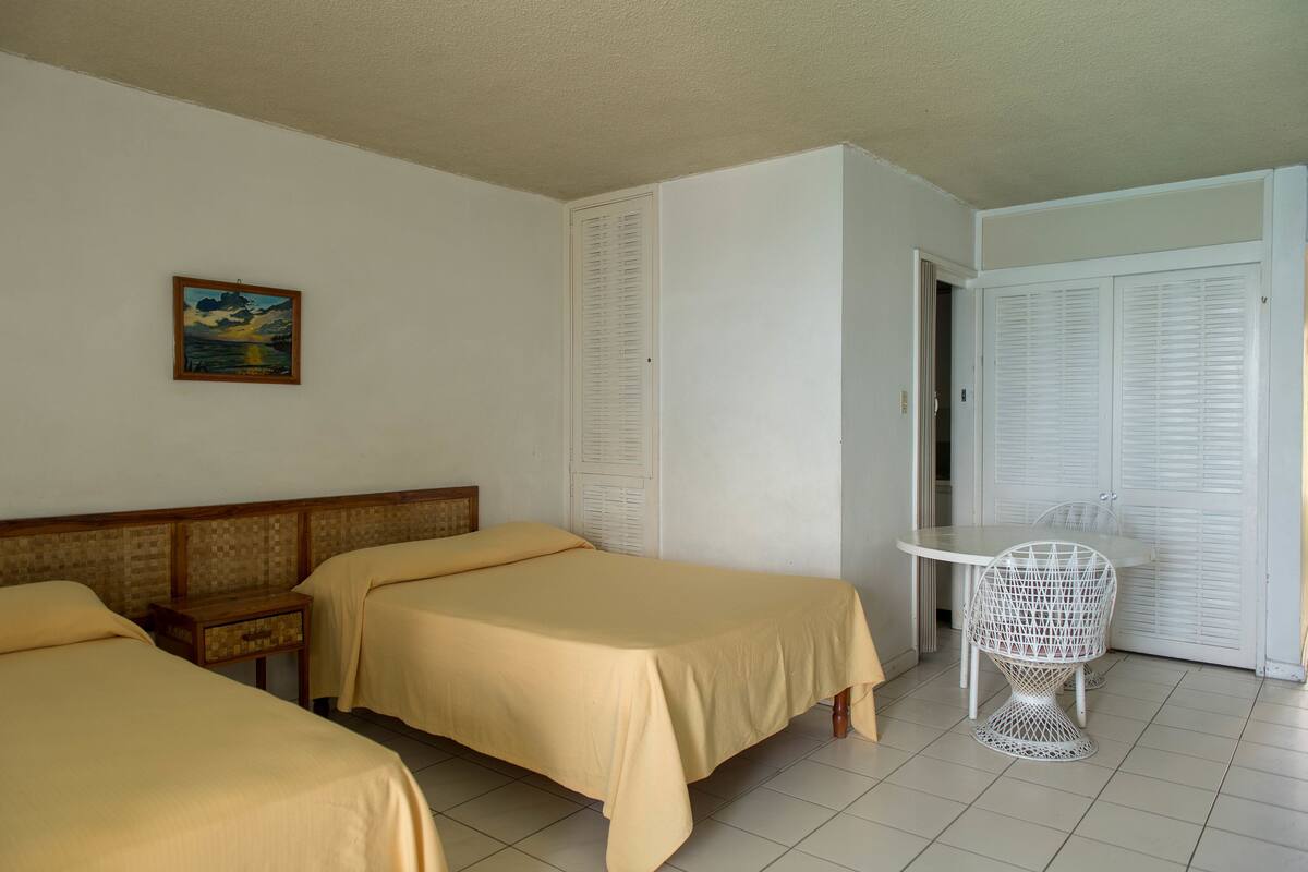 A hotel room with two beds, a small table, a chair, and a wardrobe.