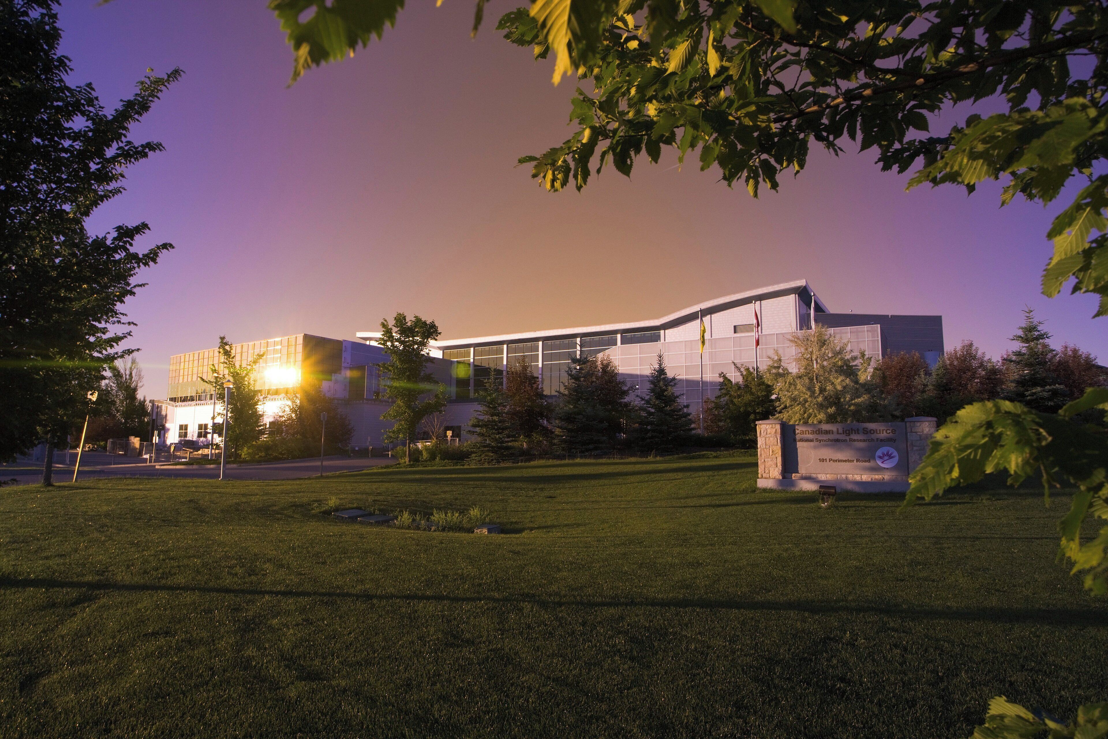 A modern building with a glass facade, surrounded by a grassy area and trees.