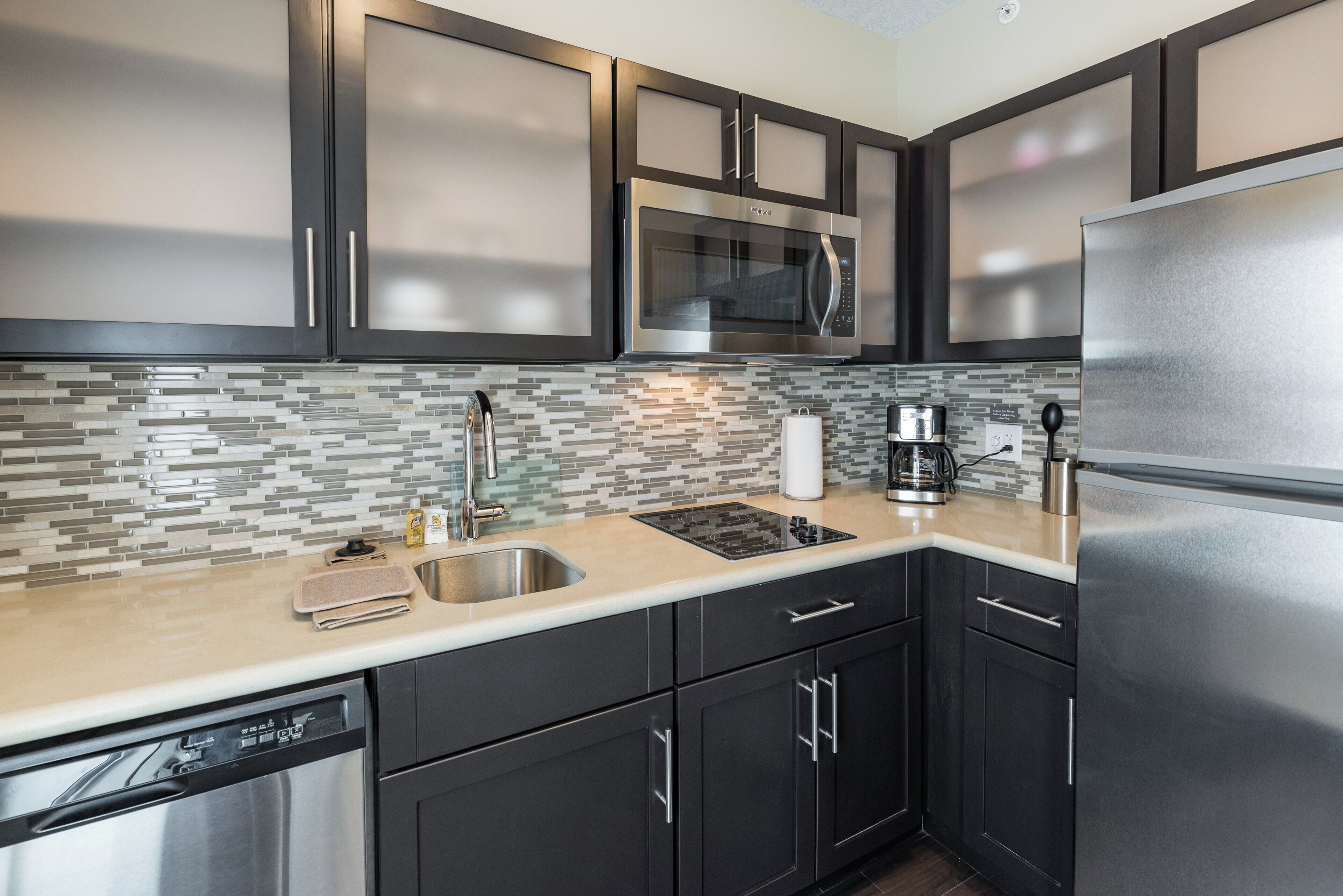A modern kitchen with stainless steel appliances, a tiled backsplash, and dark cabinetry.