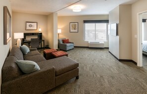 Ein Hotelzimmer mit Sofa, Ohrensessel, kleinem Tisch, Schreibtisch und einem großen Fenster.