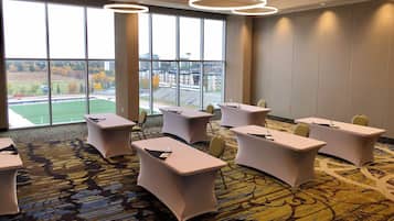 A conference room with tables and chairs, large windows with a view of a sports field, and a patterned carpet.