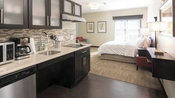 A modern hotel room with a kitchenette, a bed, a desk, and a window with a view.