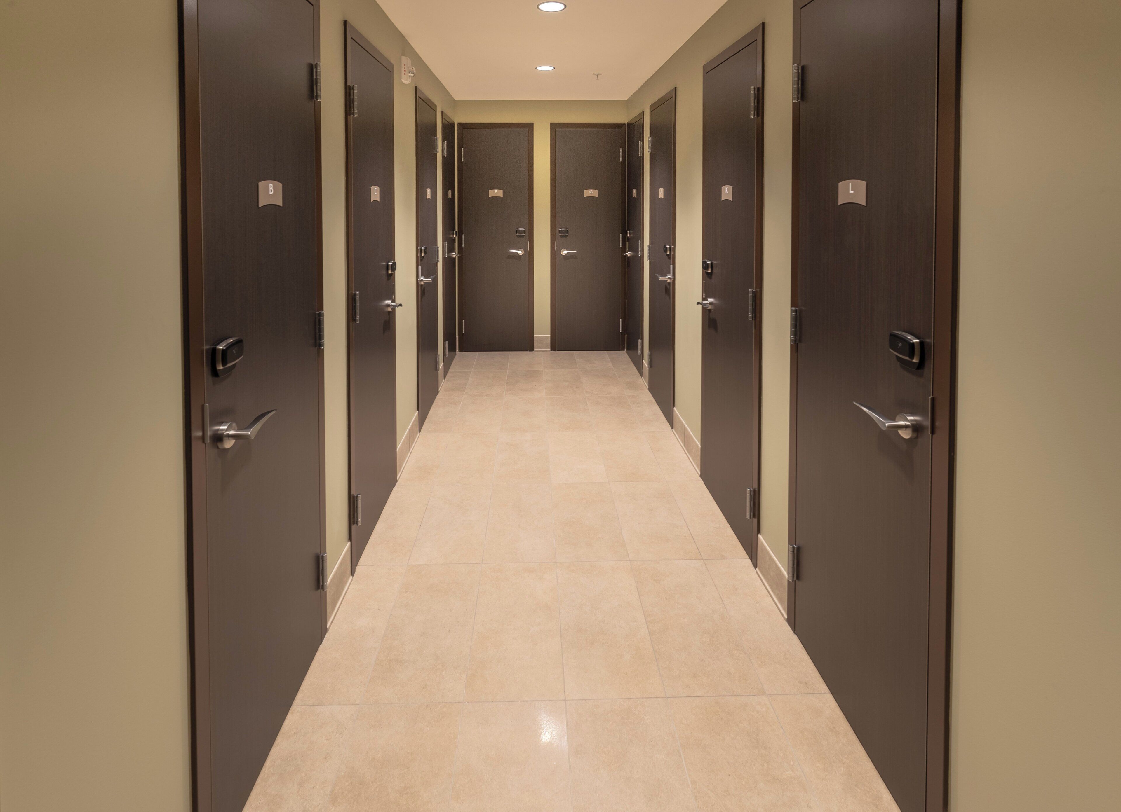 Un couloir bordé de nombreuses portes, chacune étant marquée d’une lettre, et donnant sur des pièces individuelles.