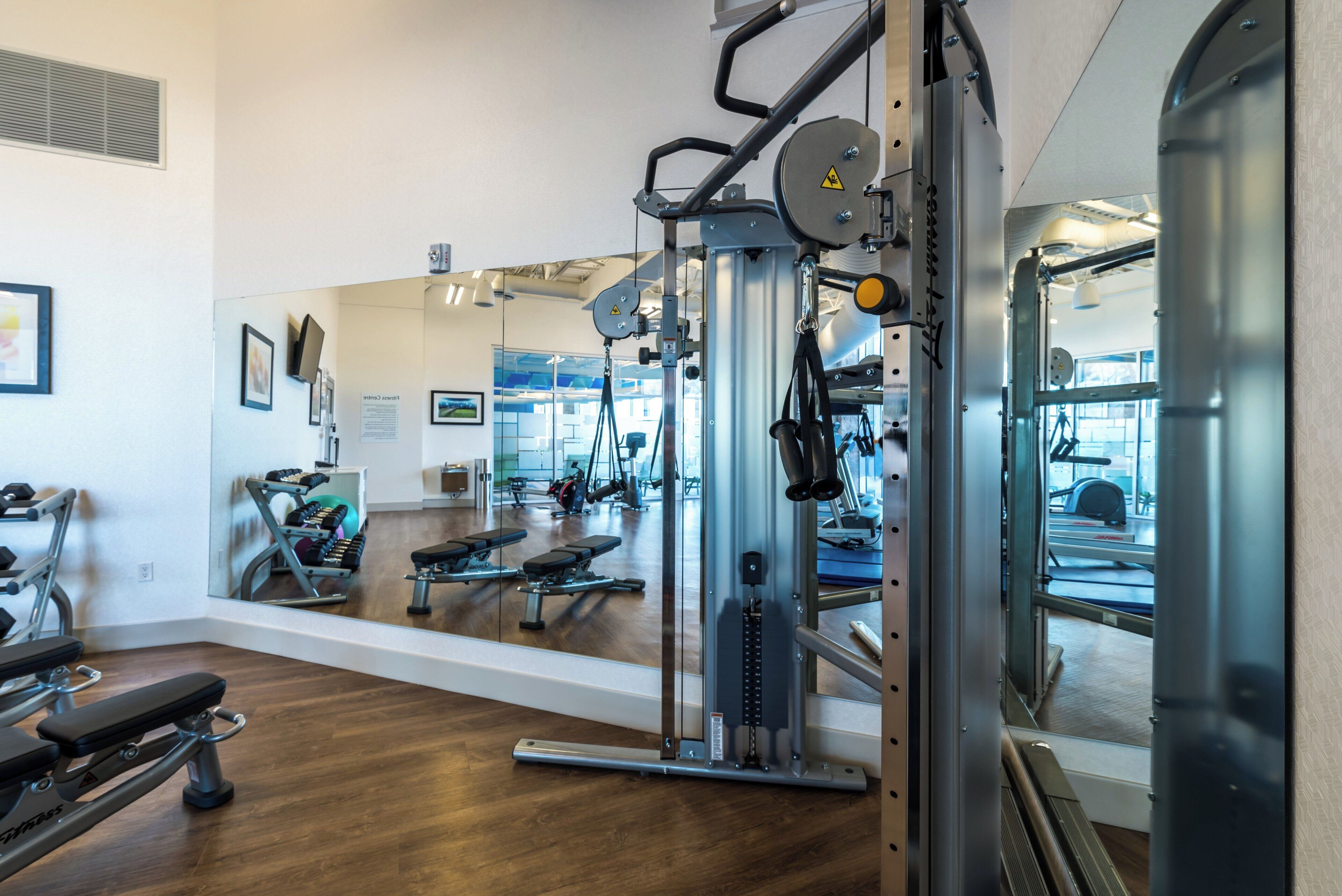 Ein Fitnessraum mit Trainingsgeräten, einem Spiegel und einem Holzboden.
