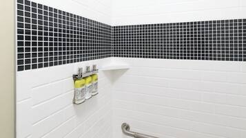 Ein Badezimmer mit weißen Fliesen im U-Bahn-Stil, einer schwarz-weißen Mosaik-Spritzschutzwand und einer Handstange.