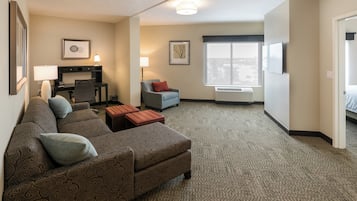 Habitación de hotel con sofá, dos mesitas auxiliares, escritorio con silla, ventana con vistas y televisor de pantalla plana montado en la pared.