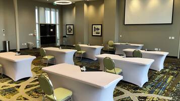 A conference room with white tables and chairs, a projector screen, and a patterned carpet.