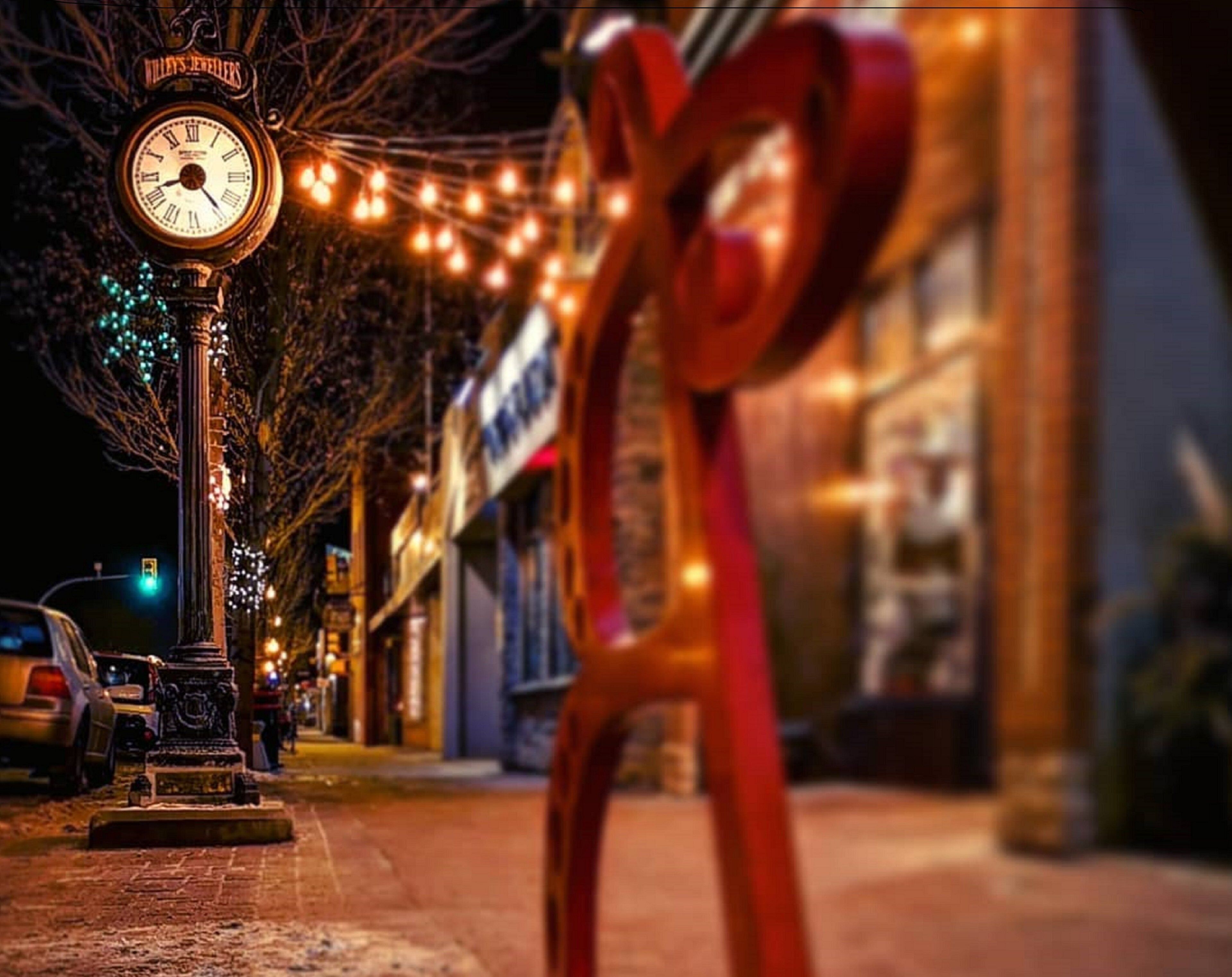 A street scene with a clock, a red bow decoration, and a building with lights.