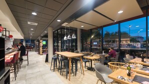 Un restaurant moderne doté de hauts plafonds, d’un éclairage suspendu et de grandes fenêtres offrant une vue sur le paysage urbain.