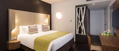 A modern hotel room with a large bed, bedside tables, a desk, and a chair.