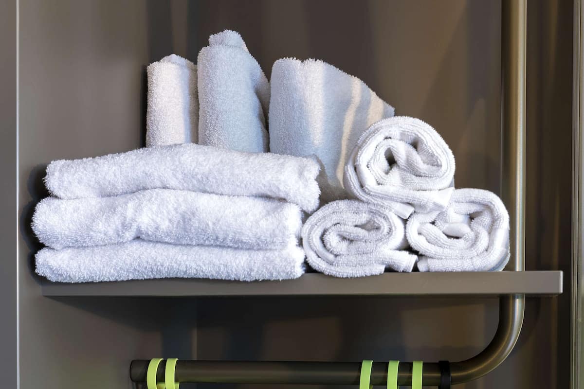 Ein Badezimmer mit Handtuchhalter, gefaltete Handtücher und einer Ablage mit aufgerollten Handtüchern.
