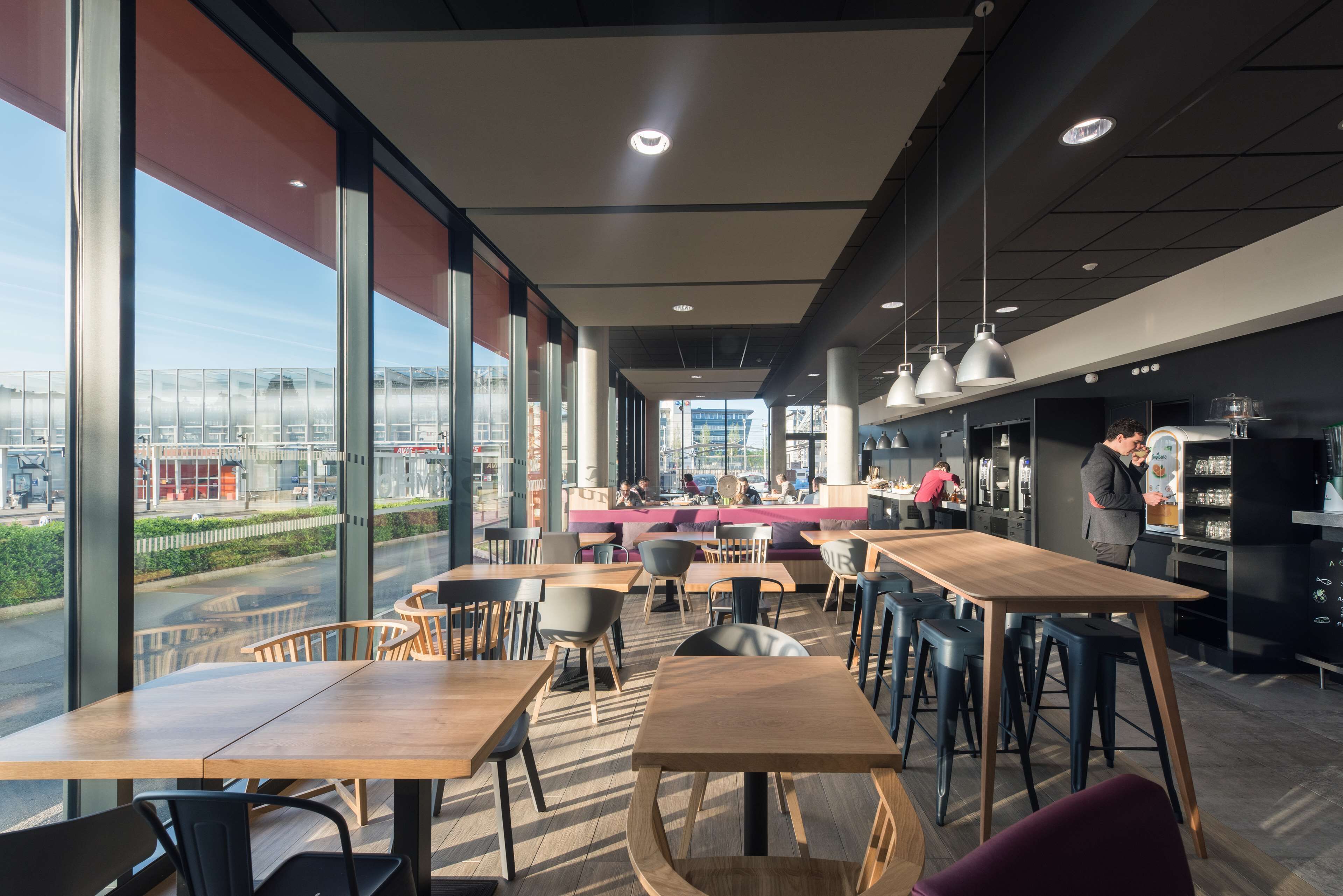 Een modern café met grote ramen, houten tafels en een bar.