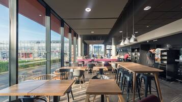 A modern cafe with large windows, wooden tables, and a bar area.