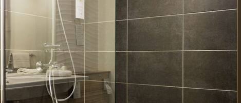 A modern bathroom with a glass-enclosed shower, dark tiled walls, and a visible sink area.