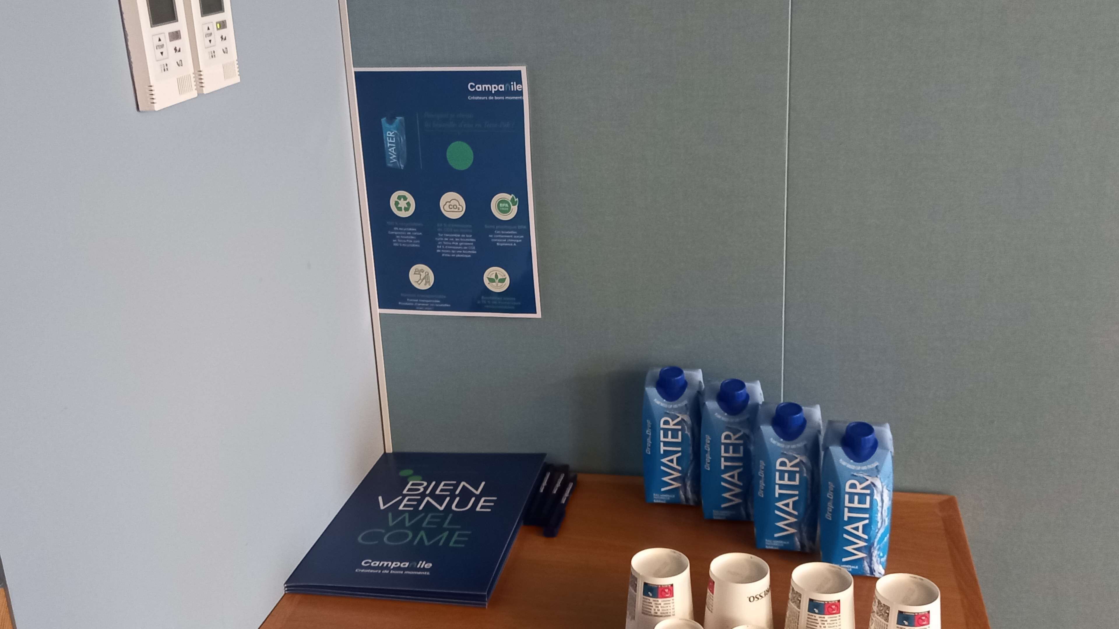 Une table avec des bouteilles d’eau, une brochure et une affiche accrochée au mur.