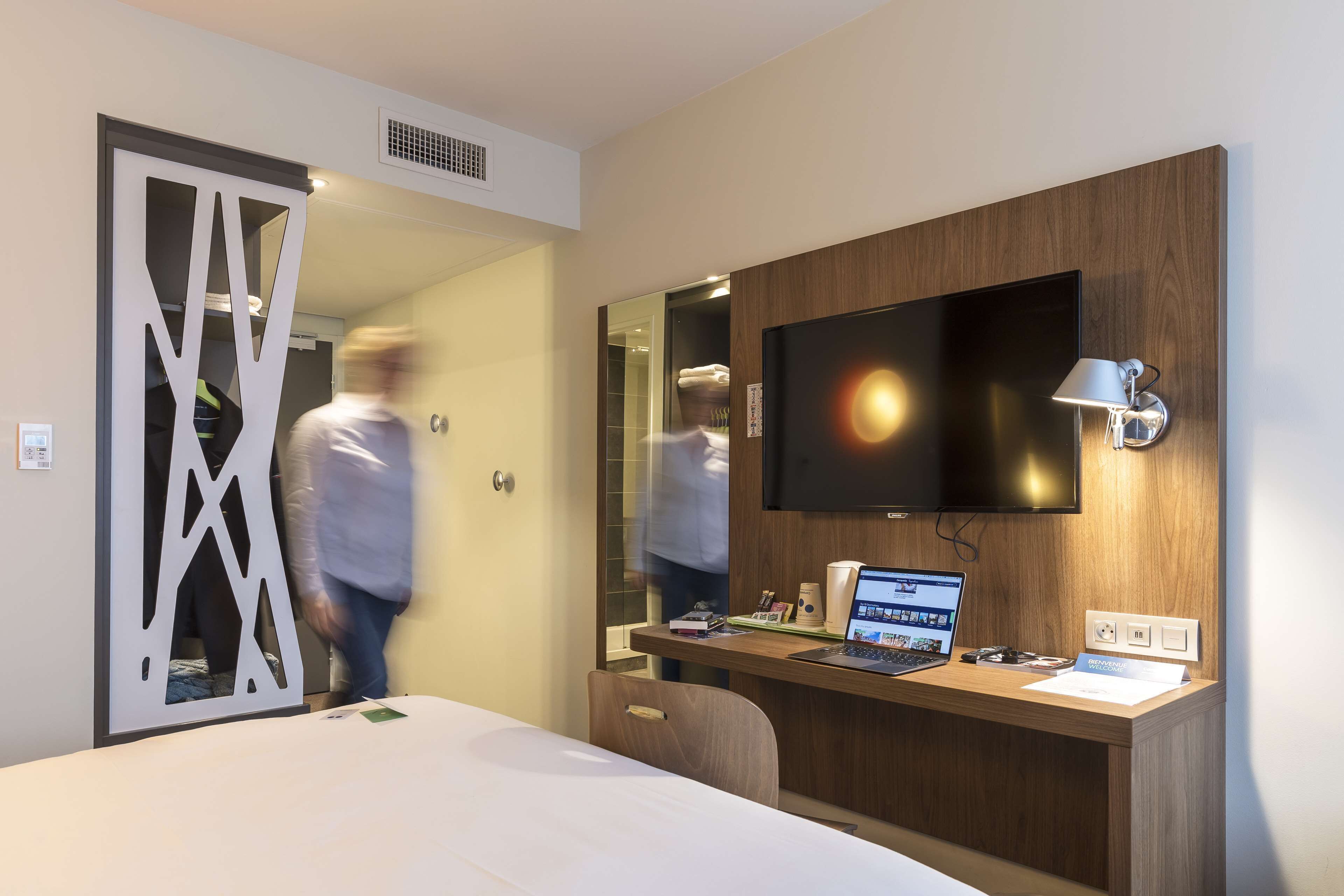 Une chambre d’hôtel équipée d’un lit, d’un bureau avec un ordinateur portable, d’une télévision à écran plat et d’un miroir.