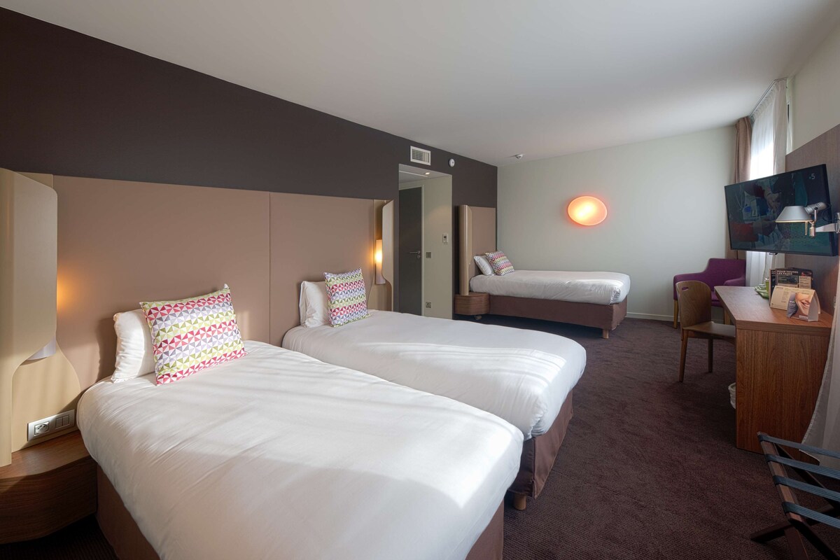 Ein Hotelzimmer mit zwei Betten, einem Schreibtisch, einem Stuhl und einem Fernseher.