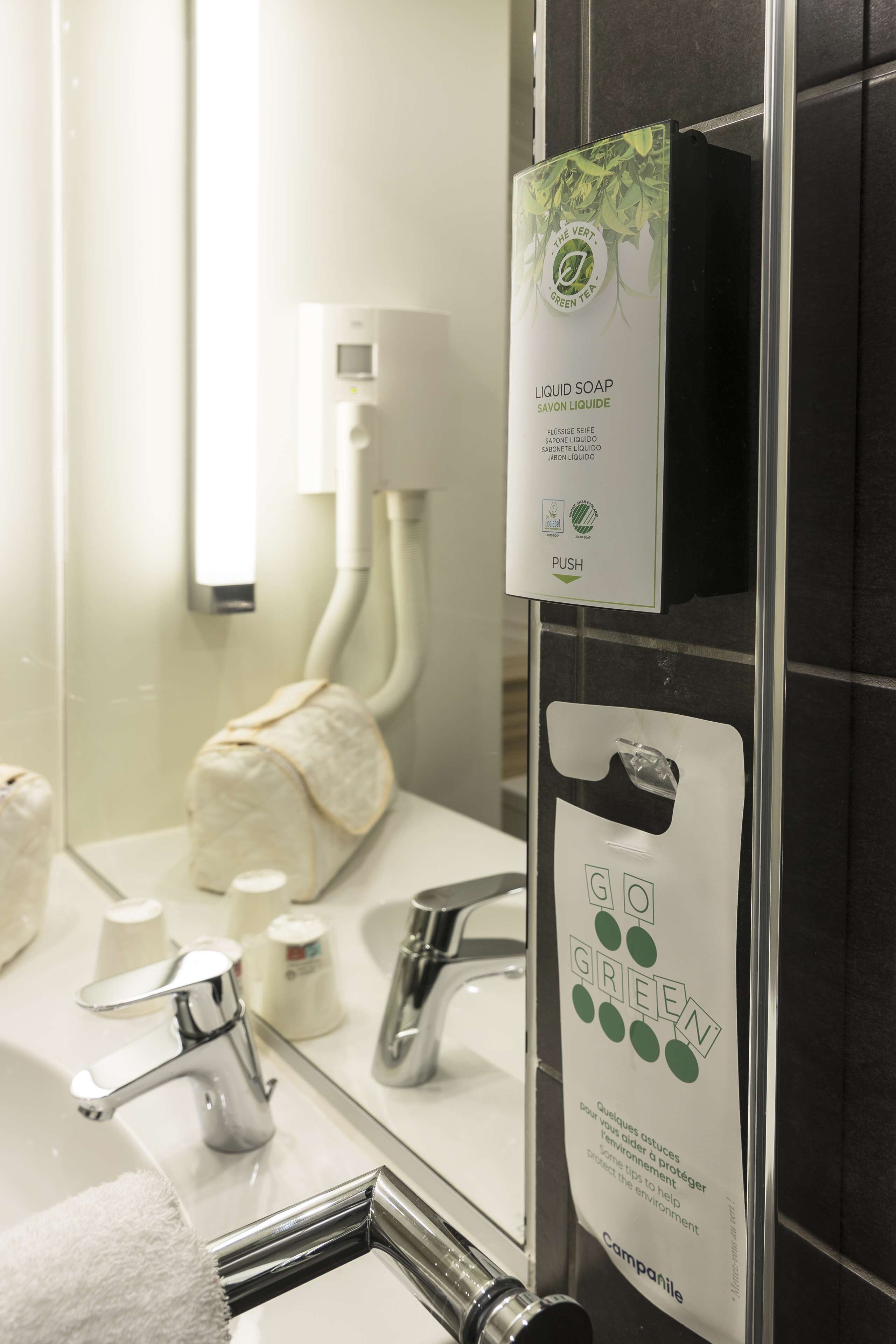 Une salle de bain avec un miroir, une serviette, un distributeur de savon et un autre distributeur de savon avec une étiquette verte.